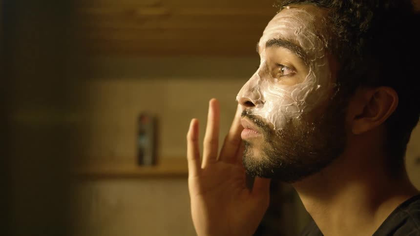 A man applies a thick lotion to his face with his fingers