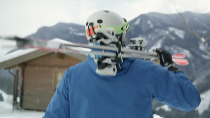 A skier hiking in snowy mountains with a pair of skis on their shoulder