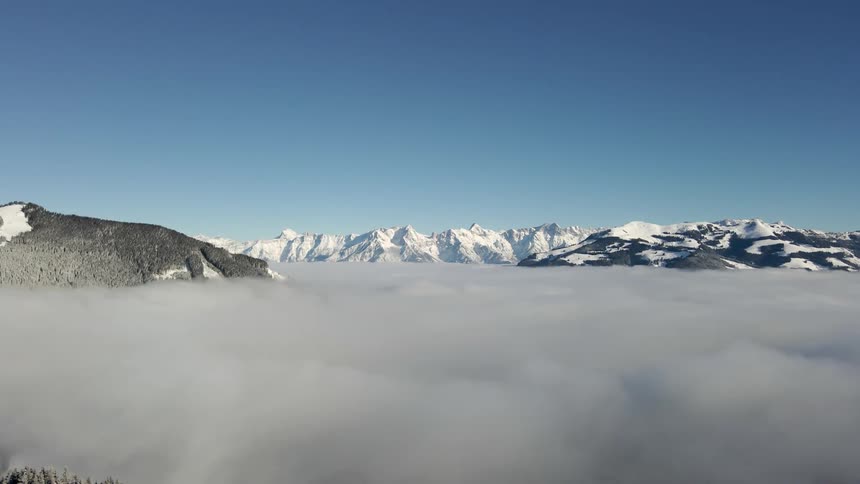 Aerial view of the snow covered peaks of a mountain range over the clouds at daytime
