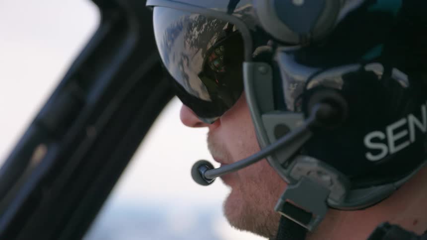 Helicopter pilot wearing a helmet flies a helicopter over the snow covered peaks of a mountain range