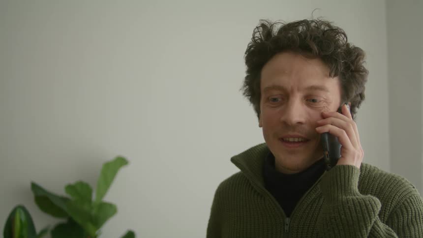 Happy man in a sweater talking on a cell phone indoors