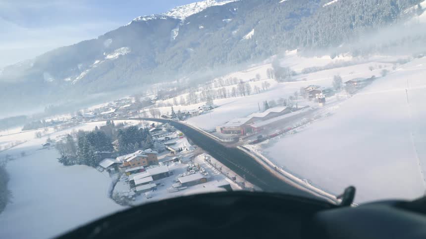 An airplane flies over the snow covered land and buildings