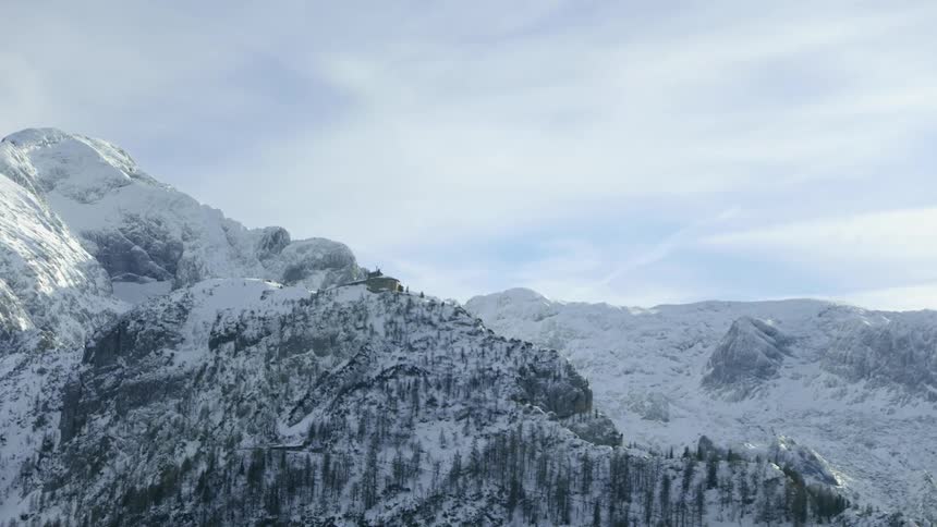 A building sits atop a mountain ridge covered with snow and trees