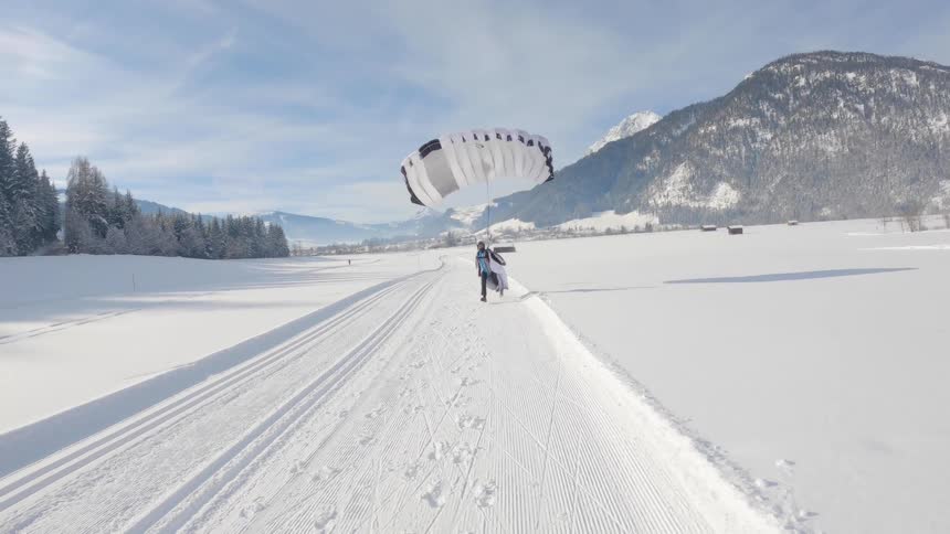 Paraglider landing on a snowy field near the mountains