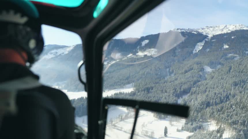 A man piloting a helicopter over the forest in the snow covered mountain range