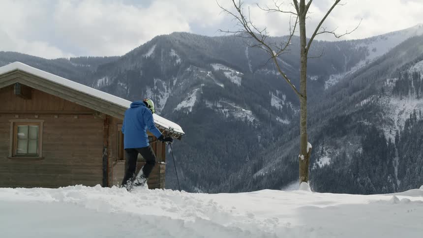 A person with a helmet and coat putting down skis on the snow with a mountain range the sky and clouds in the background