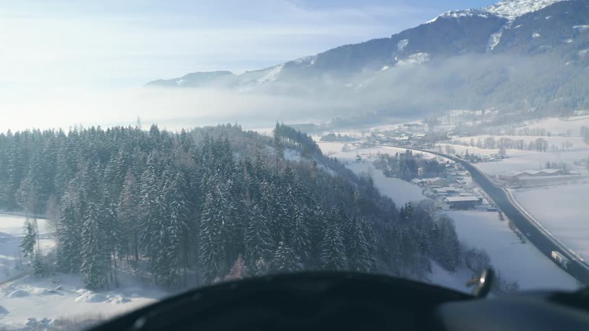 A helicopter flying over trees snow mountain and road