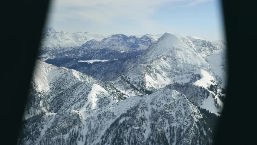 A snowy mountain range outside the window of an aircraft on a sunny day
