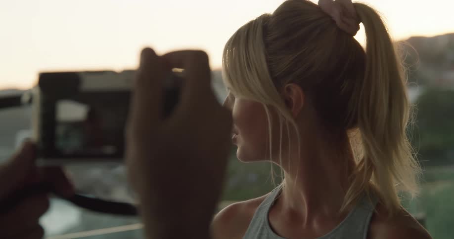 A blonde woman posing outside for a photographer with a camera