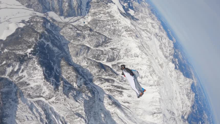A person gliding through the air over snowy mountains on a winter day