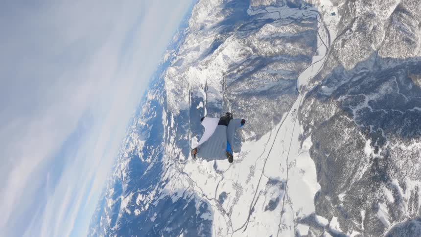 Skydiver wearing a wing suit is floating and gliding over a snow covered mountain range