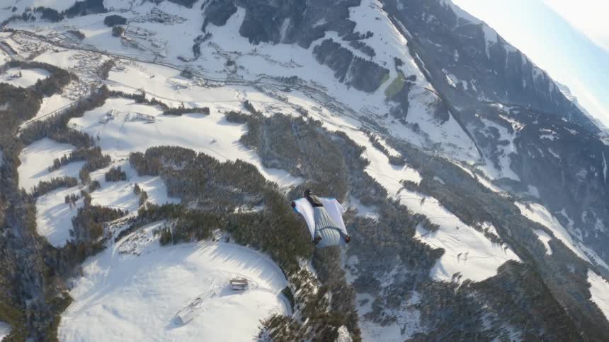 A person in a wingsuit flies over ground near a mountain range