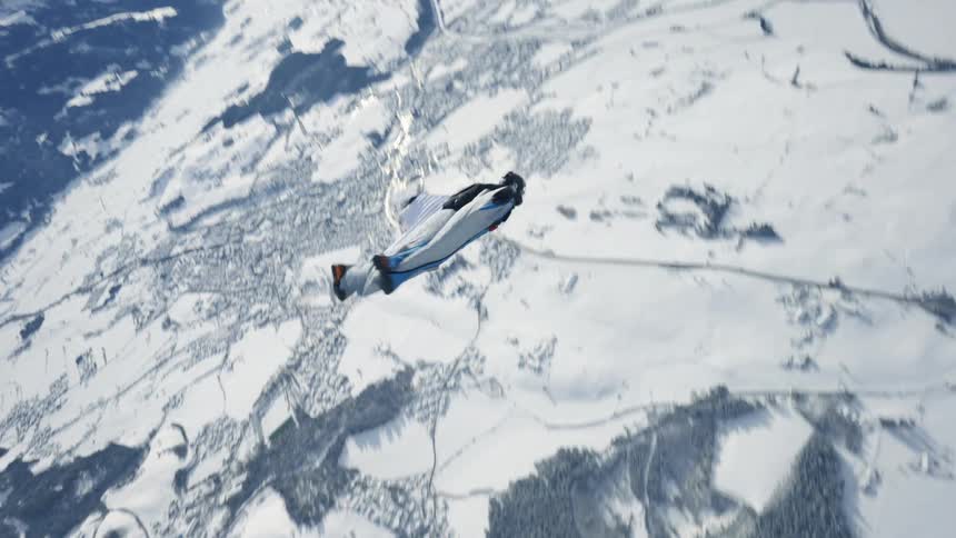 Aerial footage of a skydiver wearing a wingsuit falling over the snow covered peaks of a mountain range
