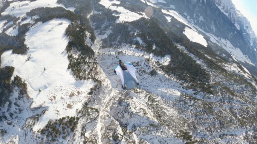Skydiver wearing a wing suit is floating and gliding over a snow covered mountain range