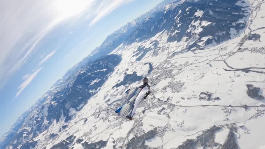 Skydiver wearing a wing suit is floating and gliding over a snow covered mountain range
