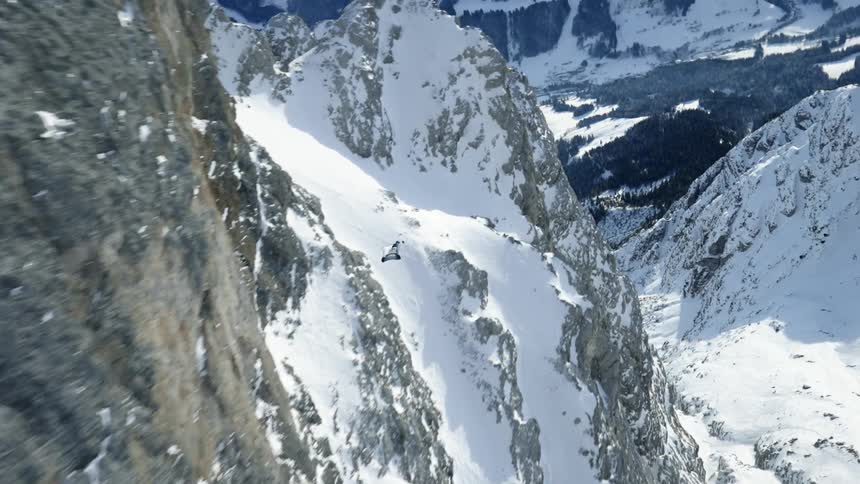 Skydiver wearing a wing suit is floating and gliding over snow covered mountains
