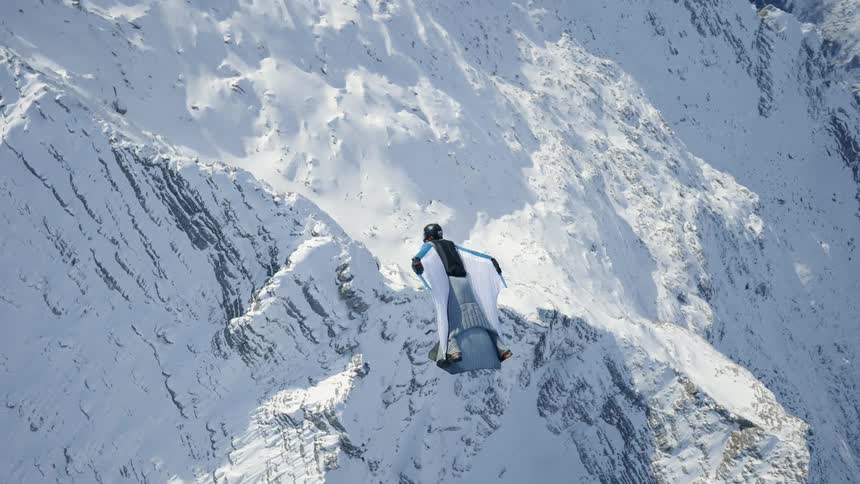 Wingsuit flyer gliding across snow capped peaks in the mountains