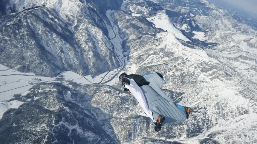 Skydiver wearing a wing suit is gliding over snow covered mountains