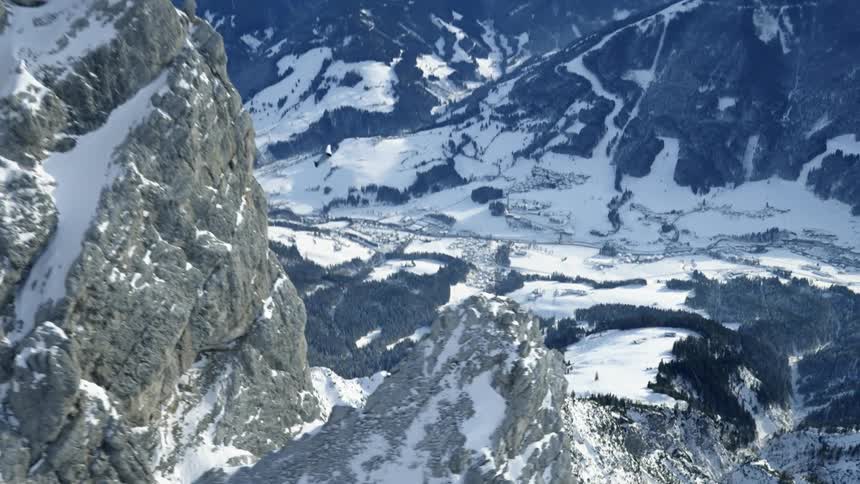 Skydiver wearing a wing suit is floating and gliding over snow covered mountains