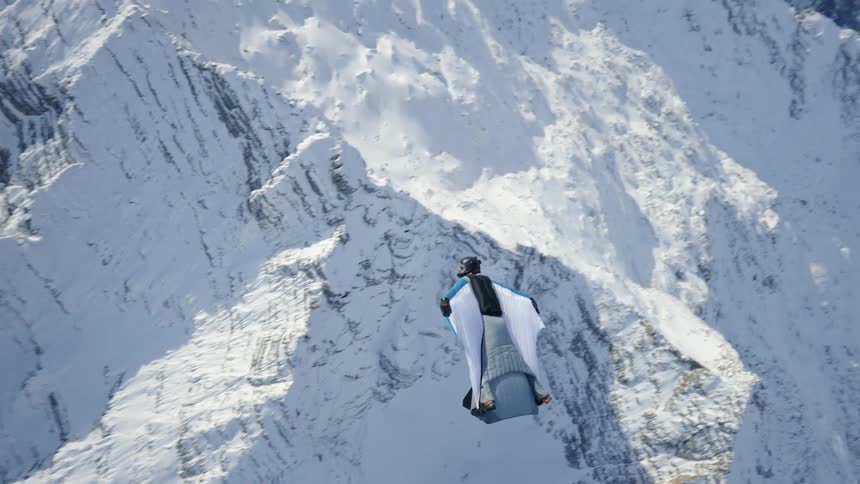 Skydiver wearing a wing suit is floating and gliding over snow covered mountains