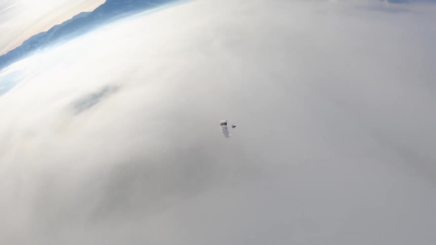 Aerial view of a skydiver gliding on a parachute over the clouds covering the mountains