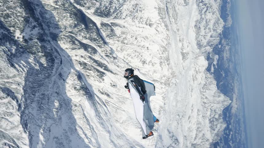 Skydiver wearing a wing suit is gliding over snow covered mountains
