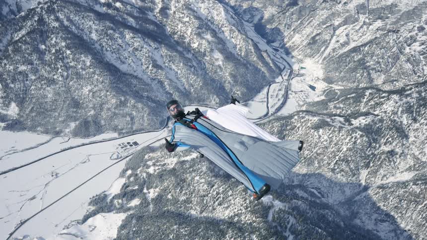 Skydiver wearing a wing suit is floating and gliding over a snow covered mountain canyon