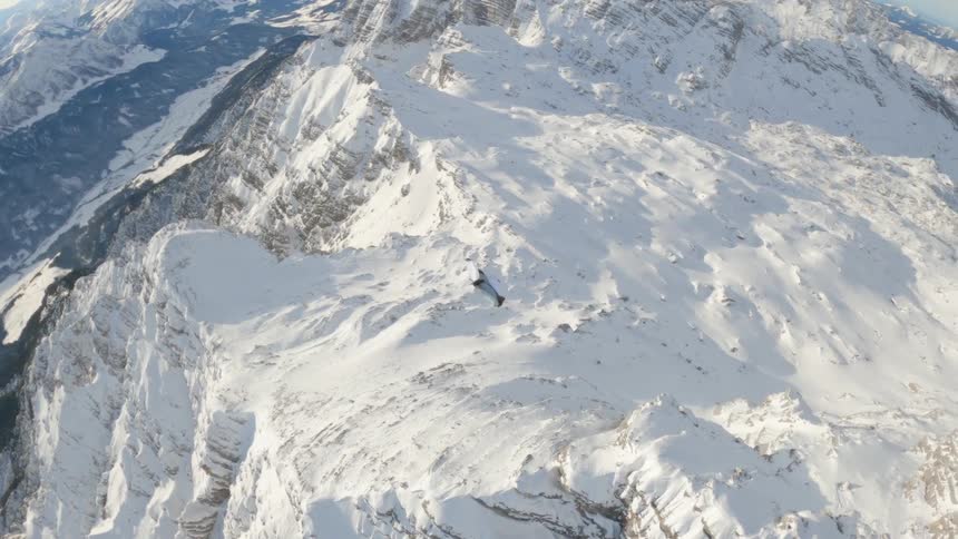 Skydiver wearing a wing suit is gliding over snow covered mountains