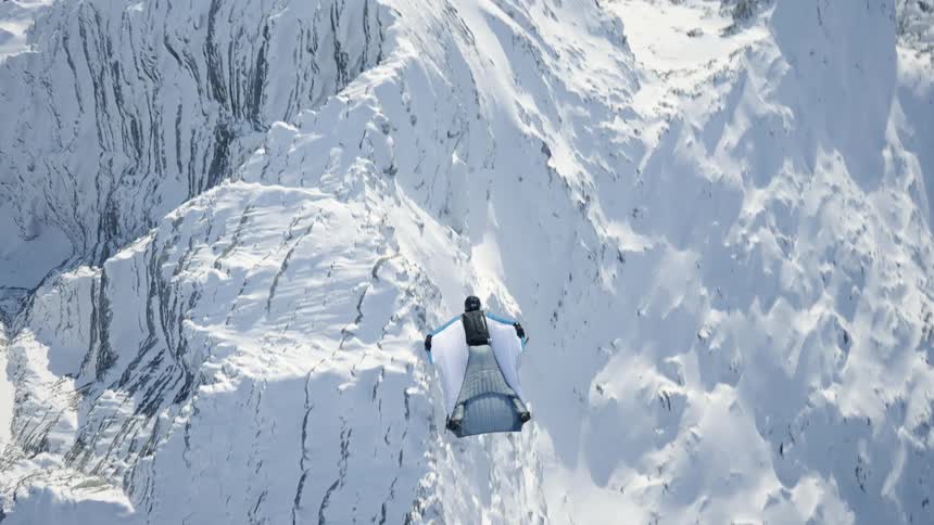 Skydiver wearing a wing suit is gliding over snow covered mountains