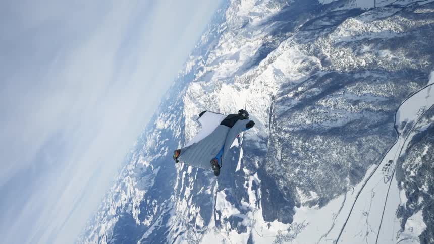 Skydiver wearing a wing suit is floating and gliding over snow covered mountains