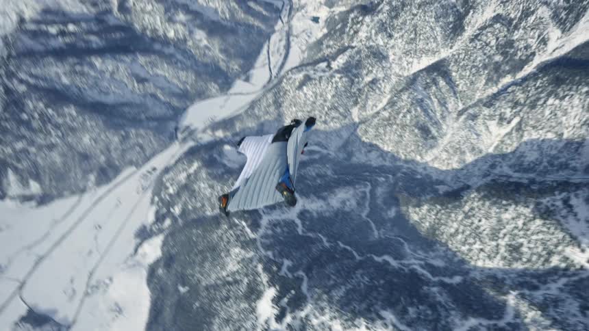 Skydiver wearing a wing suit is floating and gliding over a snow covered mountain canyon