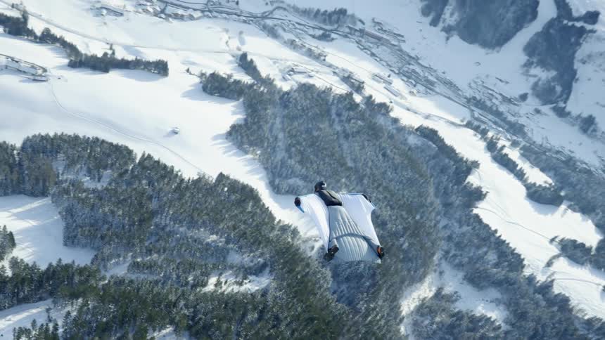 A person gliding through the air over snowy mountains in winter