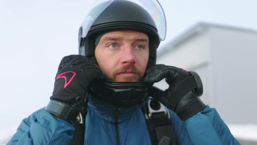 A man adjusts a helmet on his head while standing outside during the day