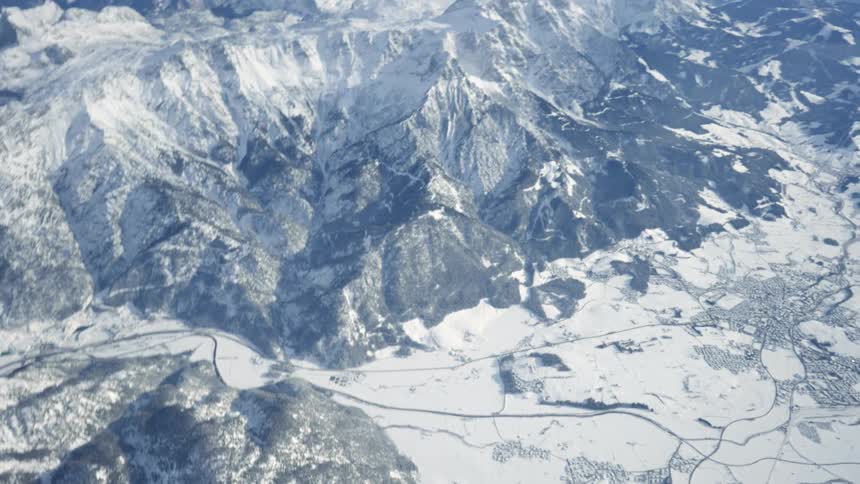 Man stepping out of a helicopter flying over the snow covered peaks of a mountain range