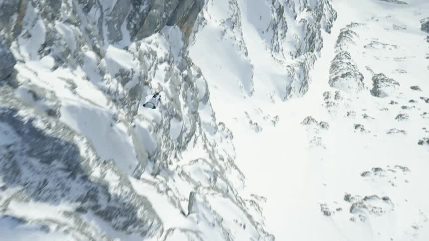Skydiver wearing a wing suit is gliding over snow covered mountains