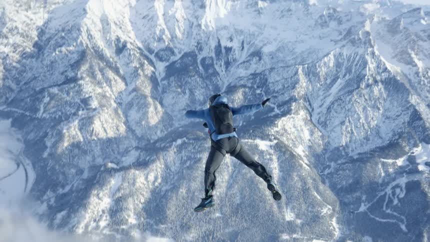A skydiver falls with their limbs spread wide in the sky over a snowy mountain range during the day