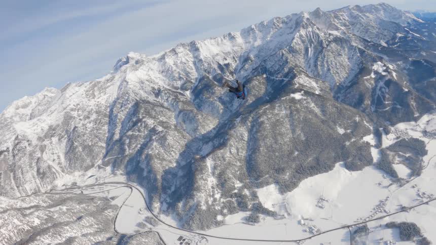 A skydiver spreads his arms and legs as he flies near a snow covered mountain range