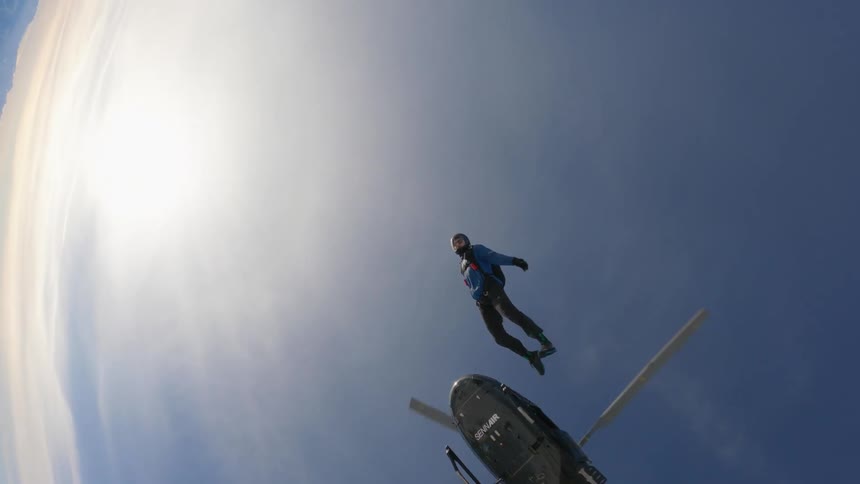 Skydiver jumps from a helicopter over the snow covered peaks of a mountain range