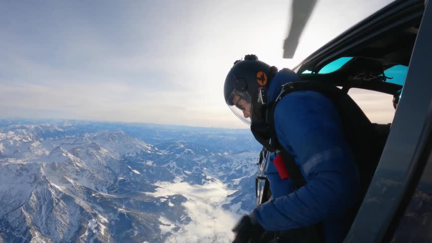A person leaning out a helicopter over some mountains getting ready to skydive