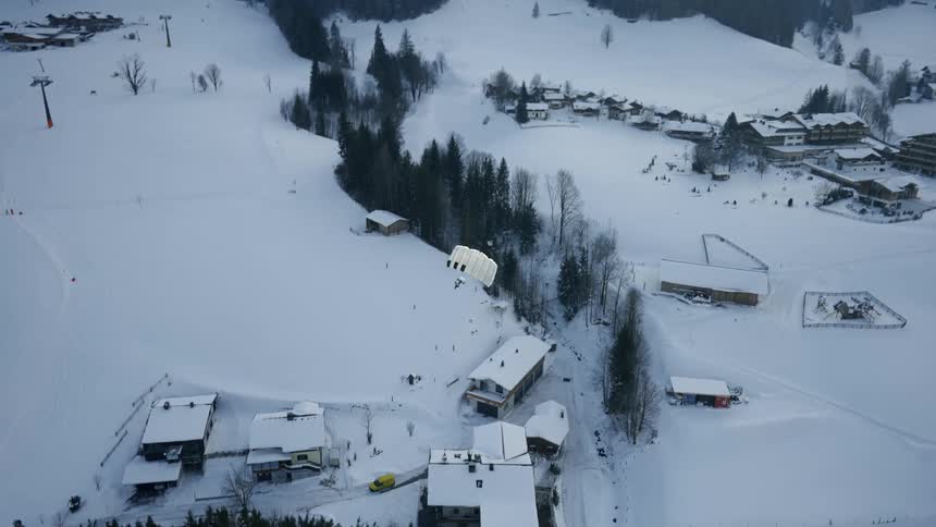 A skydiver has their parachute open as they slowly descend towards the snow covered ground below