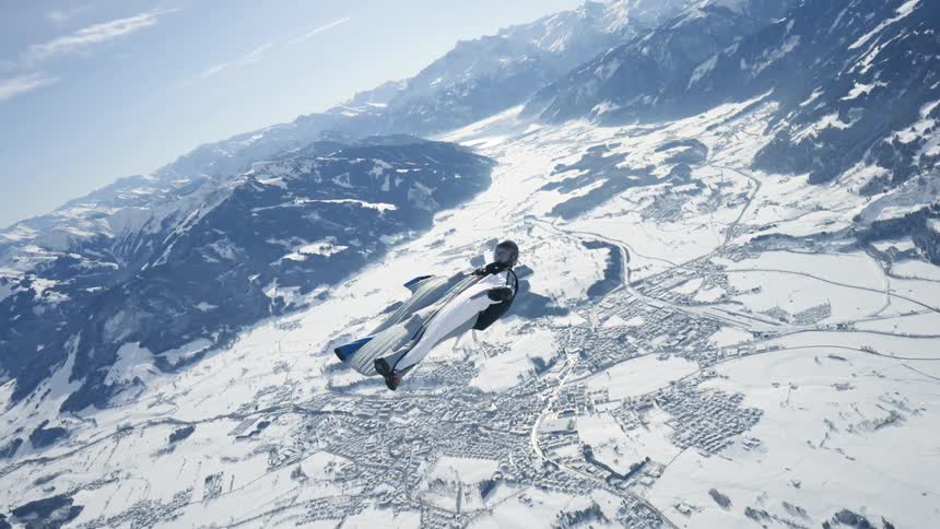 Skydiver wearing a wing suit is floating and gliding over a snow covered mountain canyon