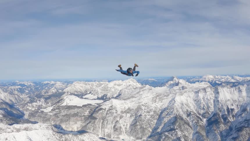 A skydiver adjusts and moves his arms back and forth as he flies over a mountain range