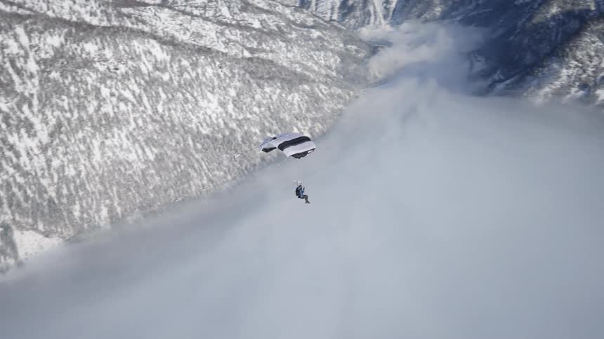 A person paragliding with a mountain range the sky and clouds in the background