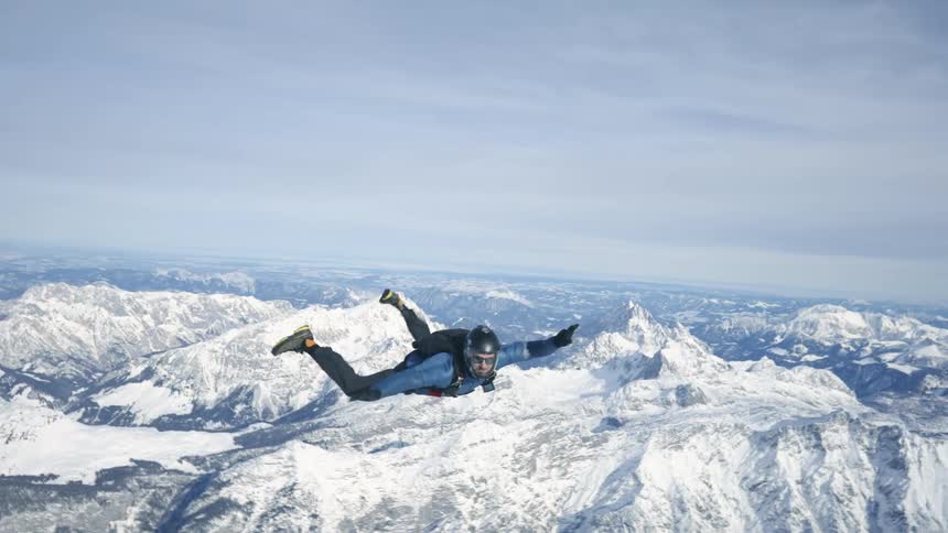 Aerial footage of a skydiver falling over the snow covered peaks of a mountain range