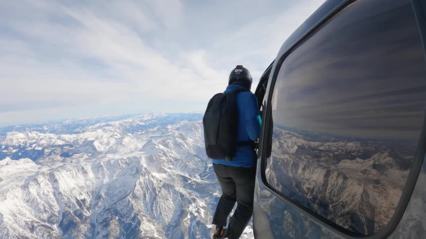 A man climbing out of a helicopter onto the rails next to it while it is flying