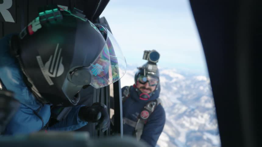 Skydiver wearing a helmet signals a friend hes ready to jump out of a helicopter over the snow covered mountains