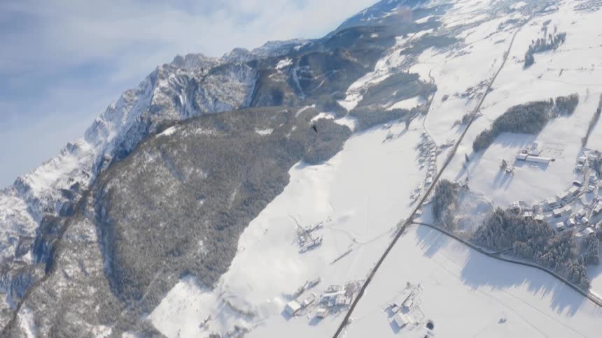 Person wearing a parachute is gliding over snow covered mountains and mountain canyon