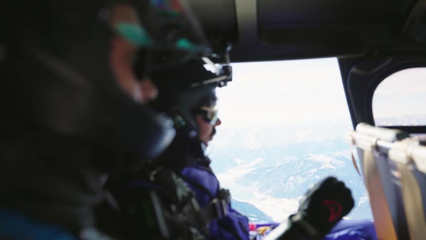 Two men with helmets and gloves in an aircraft with a man with a camera on his helmet