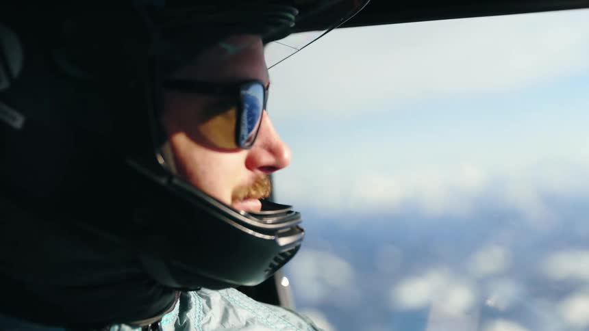 Man wearing a helmet and sunglasses flying on an airplane over the snow covered mountains