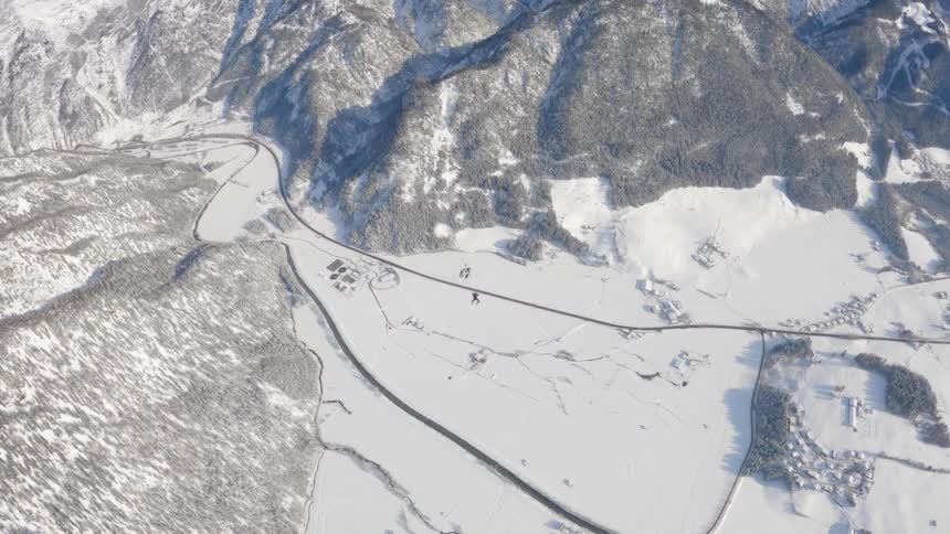 Skydiver who is wearing a wing suit is floating and gliding over a snow covered mountain canyon as they open their parachute and move higher into the sky